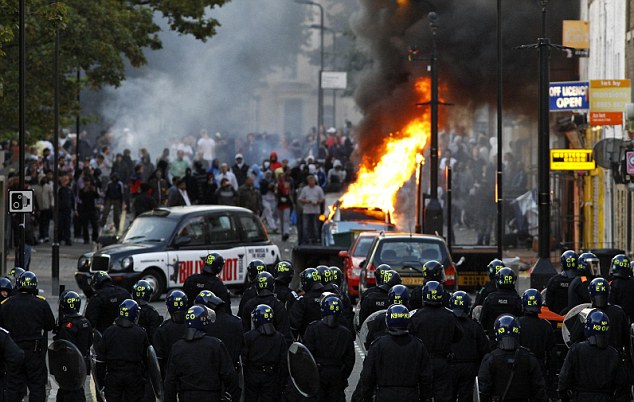 Police officers in riot gear block a road near a burning car on a street in Hackney, east London August 8, 2011. Youths hurled missiles at police in northeast London on Monday as violence broke out in the British capital for a third night. REUTERS/Luke MacGregor (BRITAIN - Tags: CIVIL UNREST CRIME LAW IMAGES OF THE DAY)