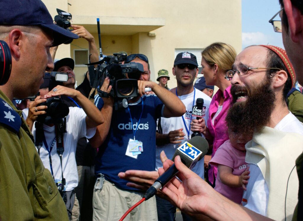[בכרזה: ההתנתקות - עוד מהלך כזה ואבדנו... תושב הישוב מורג מתעמת מילולית עם אנשי כוחות הביטחון הבאים לפנותו. קרדיט: MARK NEYMAN, לע"ם]