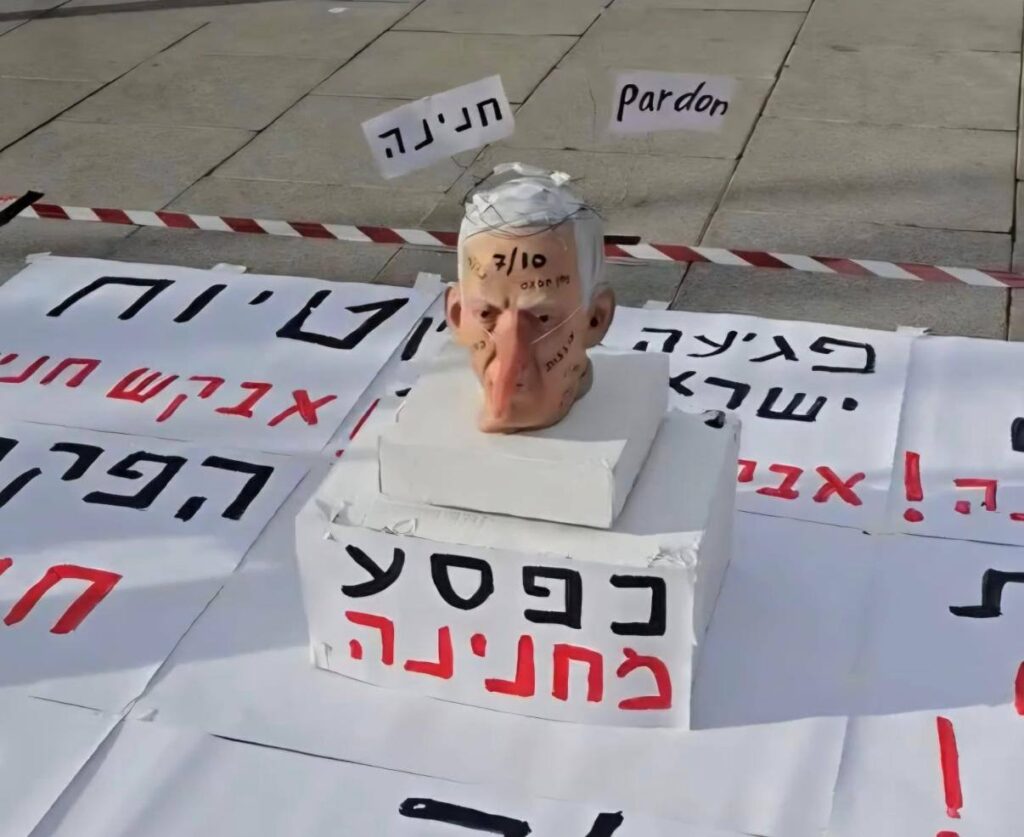 [בתמונה: מיצג עם ראשו הכרות של בנימין נתניהו מחוץ לבית המשפט, ב- 9 בדצמבר 2025. התמונה שותפה הרבה ברשתות החברתיות ובעל הזכויות שבה לא אותר. לכן, השימוש נעשה לפי סעיף 27א' לחוק זכויות יוצרים.  בעל הזכויות הראשי, אנא פנה ל: yehezkeally@gmail.com]